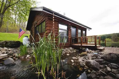 a log cabin with a pond in front of it at Lake with Dock and Hot Tub Hocking Hills Cabin in Rockbridge