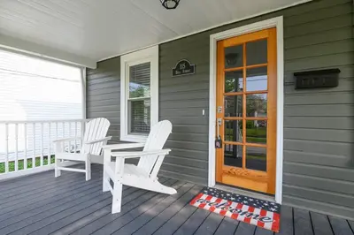 a porch with two white chairs and a wooden door at Bell Street by the Falls in Chagrin Falls