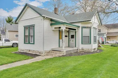 a white house with a porch and a grass yard at Enchanting Bungalow - 2BR Historic Hidden Gem in Xenia