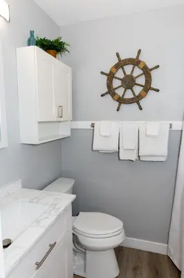 a white bathroom with a toilet and a ship wheel on the wall at Downtown Waterfront Escape in Sandusky