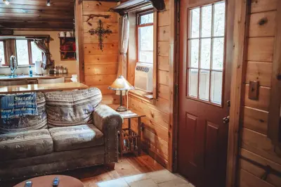 a living room with a couch and a table and windows at Great Frontier Cabin at American Heartland Cabins in Rockbridge