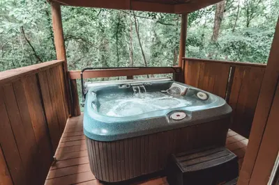 a jacuzzi tub on a deck in the woods at Great Frontier Cabin at American Heartland Cabins in Rockbridge
