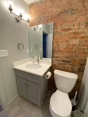 a bathroom with a white toilet and a brick wall at BUBBLES FANTASY SUITE Explore OTR and Rhinegeist in Cincinnati