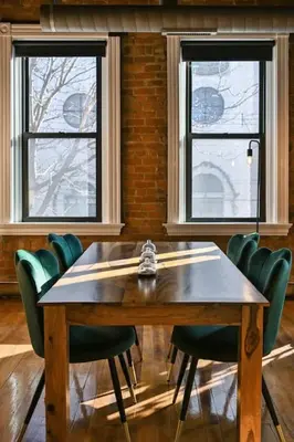 a wooden table with green chairs and two windows at Stunning Loft in the heart of OTR in Cincinnati