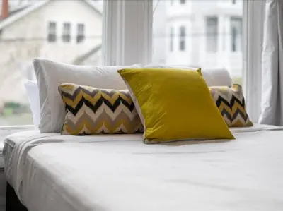 a bed with yellow and white pillows and a window at Cozy 1BR Near Zoo, UC, OTR, Downtown in Cincinnati