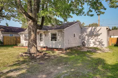 a white house with a tree in the yard at Downtown Russells Point Cottage Near Indian Lake! in Russells Point