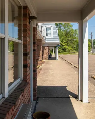 a porch of a brick house with a sidewalk at Country Squire inn and suites in Coshocton