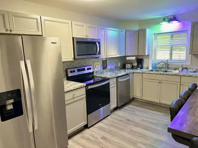 a kitchen with white cabinets and a stainless steel refrigerator at Kikis Tikis! Fun Themed Home in Vermilion