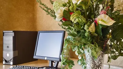 a desk with a computer monitor and a vase of flowers at Best Western Penn-Ohio Inn & Suites in Hubbard