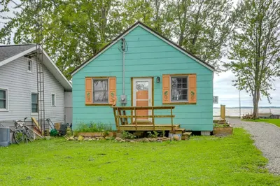 a blue house with a porch in the grass at Vickery Cottage on Sandusky Bay with Fire Pit! in Port Clinton