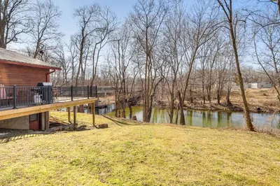 a house with a deck next to a river at Riverfront Covington Cabin with Deck and Fire Pit! in Piqua