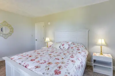 a white bedroom with a bed with a floral bedspread at Cozy Greenwich Vacation Rental with Fire Pit in Greenwich