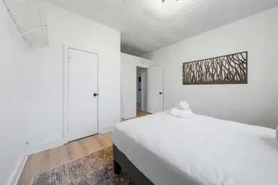 a white bedroom with a large bed and a painting on the wall at Cozy 1BR with Parking - Near UC, Zoo, Downtown in Cincinnati