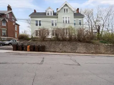 a large white house with a brick wall at Cozy 1BR with Parking - Near UC, Zoo, Downtown in Cincinnati