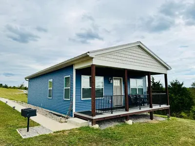 a blue house with a porch on a field at 100 Acre Relaxing Retreat Near ARK - The Cottage in Williamstown