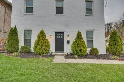 a white house with a black door and some bushes at Historic Loveland Apt Walk to Little Miami River! in Loveland