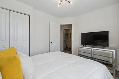 a white bedroom with a bed and a flat screen tv at Tranquil Pet Friendly Retreat residence in Reynoldsburg