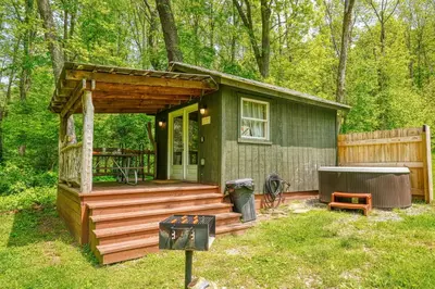 a small green cabin with a deck in the woods at Cypres Caban in Logan