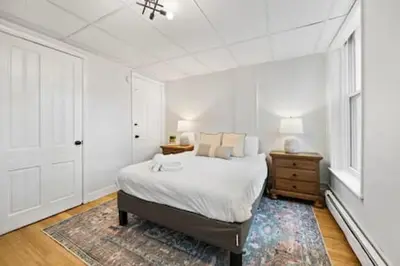 a white bedroom with a bed and a rug at Comfy 1BR with Parking - Near UC, Zoo, Downtown in Cincinnati