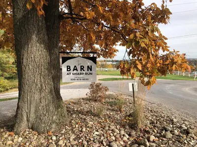 a sign that says barn at a shed dam next to a tree at The Barn at Sharp Run-Modern Barn in the heart of Amish Country in Millersburg