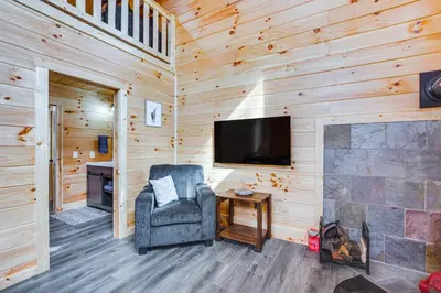 a living room with a tv and a chair and a fireplace at Modern Salineville Cabin on 13 Acres with Fire Pit! in Salineville