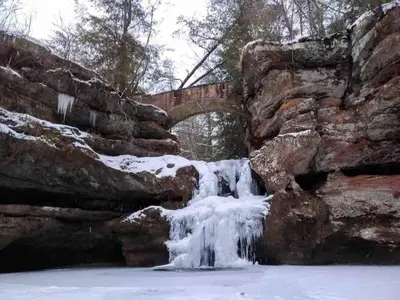 a waterfall in front of a stone wall with a bridge at 3 Bedroom in Hocking Hills w King Bed Logan Ohio in Logan