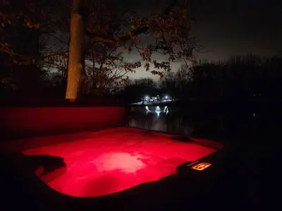 a red lighted hot tub in a pond at night at Turkey Trot, Cabin Getaway on Lake w/ Hot Tub in Streetsboro