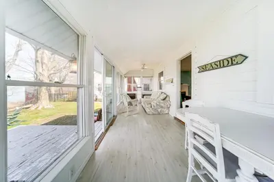a white house with a porch with a large window at Coastal Lake Erie Cottage with Amazing Water Views! in Euclid
