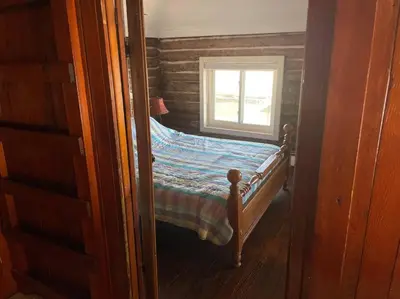a small bedroom with a bed with a window at Restored historic log cabin & deck on Lake Erie in Luna Pier