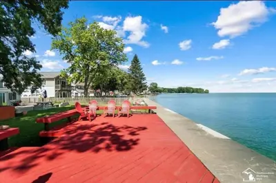a red brick walkway with chairs and tables and the water at Restored historic log cabin & deck on Lake Erie in Luna Pier
