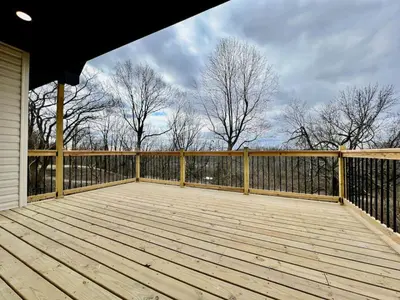 a wooden deck with a fence and some trees at Beautiful NEW Ranch Home with a large deck and games in Maud