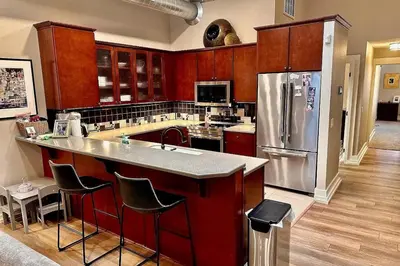 a kitchen with red cabinets and a stainless steel refrigerator at Downtown Delight with Patio! 1 Mi to Ball State in Muncie