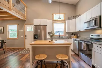 a kitchen with white cabinets and a kitchen island with stools at Nature's Nest - Woodsy Retreat w/ Renovated Deck & Hot Tub in Logan