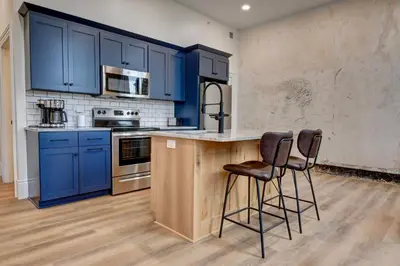 a kitchen with blue cabinets and two bar stools at Kaufman Suite- BY BUSY INTERSECTION in Millersburg
