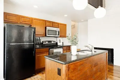 a kitchen with a black refrigerator and wooden cabinets at Soaring 2BR Parkside Loft Walkable to it All in Cincinnati