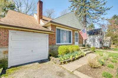 a brick house with a garage and an american flag at Cleveland Heights Home with Sunroom Park Across St! in Cleveland Heights