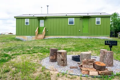 a green house with a fire pit and logs at Block of 5 Lodges at Eden Reserve - For Groups in Williamstown