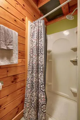 a shower curtain in a tiny bathroom with wooden walls at Blue Rose Cabins - Oleander Cabin in Logan