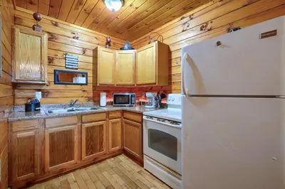 a kitchen with a white refrigerator and wooden cabinets at Blue Rose Cabins - Pine Ridge Cabin in Logan