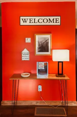 a red wall with a table with a welcome sign on it at White Oak Cabin in Argillite