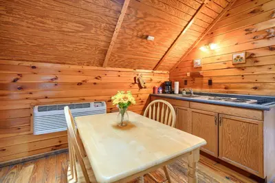 a dining room with a table and a kitchen with wooden walls at Blue Rose Cabins - Country Cottage in Logan