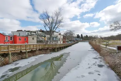 a river with snow and houses and a bridge at The Towpath Retreat-A Cozy Farmhouse Stay in Canal Fulton