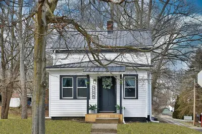 a small white house with a black door at The Towpath Retreat-A Cozy Farmhouse Stay in Canal Fulton