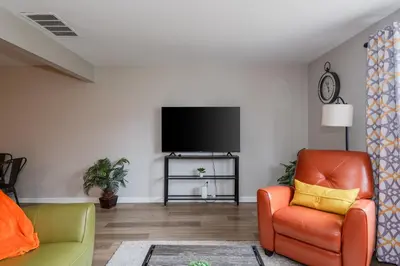 a living room with an orange chair and a flat screen tv at Modern 2BR Gem Steps to The Greene UD & WPAFB in Kettering