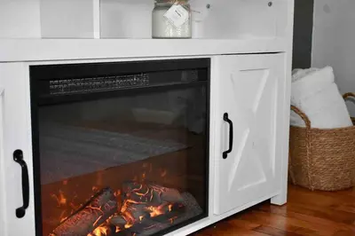 a fireplace in a white cabinet with a fire in it at Cozy Garden House in Adrian