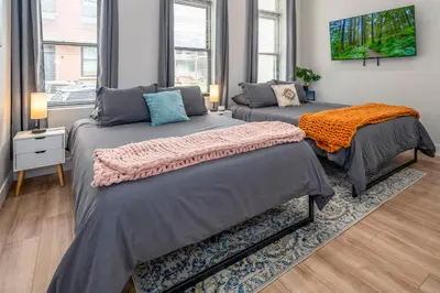 two beds in a room with two windows at Prime OTR, 3 Lux Queen Beds, Two 55in TVs, Steps to TQL, Findlay Market, Light Rail, Fast Wifi in Cincinnati