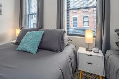 a bedroom with a bed with a blue pillow and a window at Prime OTR, 3 Lux Queen Beds, Two 55in TVs, Steps to TQL, Findlay Market, Light Rail, Fast Wifi in Cincinnati