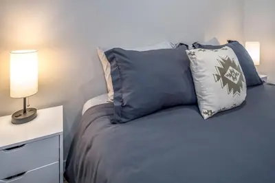 a bed with blue pillows and a table with a lamp at Central Over-the-Rhine, 3 Lux Queen Beds, Steps to TQL, Findlay Market & Light Rail, Fast Wifi, Sleeps 7ppl in Cincinnati