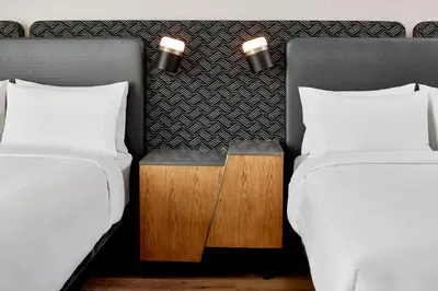 two beds with white sheets and a wooden table between them at Hotel Celare, Cincinnati Midtown, a Tribute Portfolio Hotel in Cincinnati