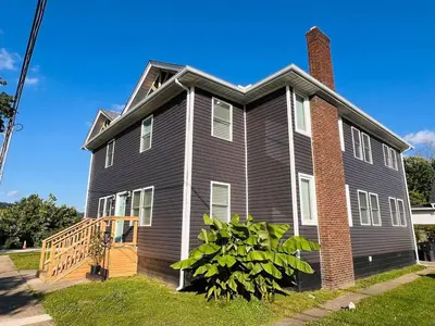 a gray house with a brick chimney and a porch at RiverSuite1 - A mesmerizing river and bridge view. in Russell
